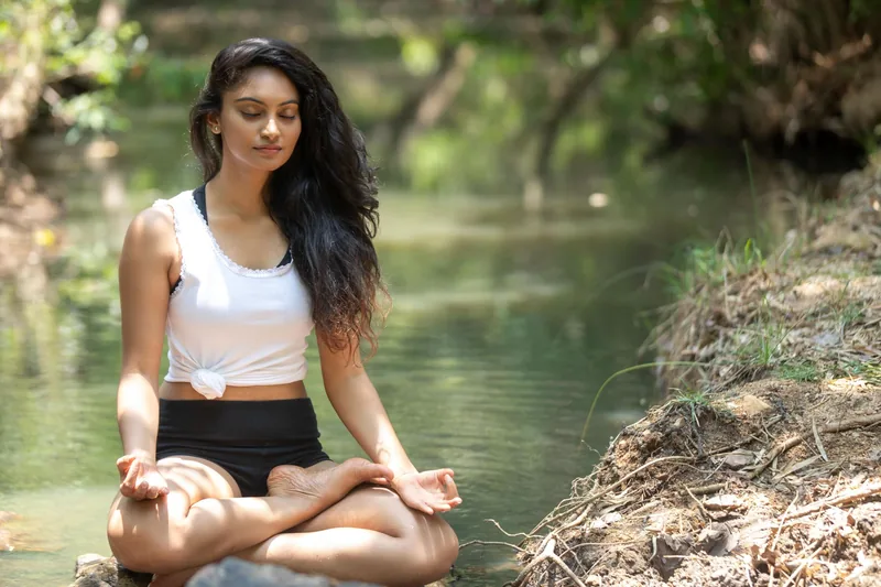 Woman practicing calm breathing and moving meditation by a river to reduce anxiety