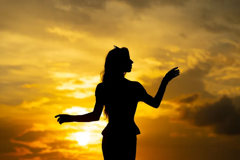 Silhouette of a woman flowing through a calming tai chi pose at sunset for stress relief