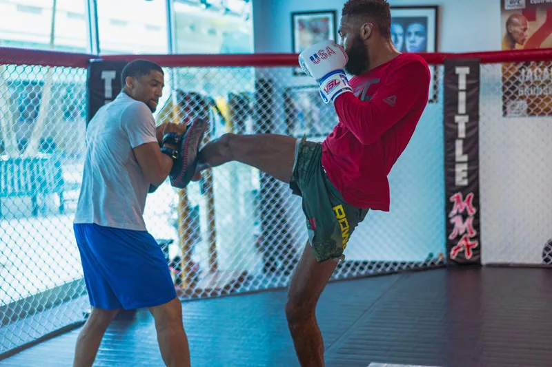 Beginner practicing striking during MMA training with a coach holding pads in the ring