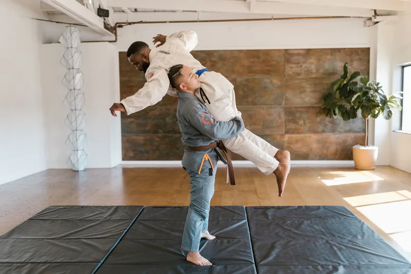 Gi-wearing jiu jitsu student lifting a partner for a throw, a BJJ takedown from the clinch