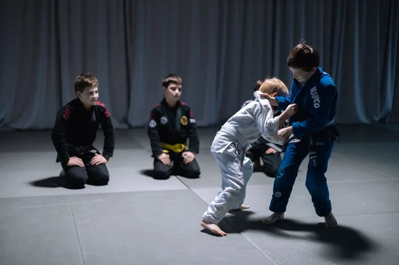 Two kids in gis drilling a jiu jitsu grip while classmates watch, the grappling side of youth MMA